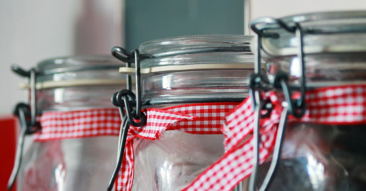 Tiga stoples kaca yang dihiasi dengan pita kotak merah, ideal untuk penyimpanan dapur atau konsep dekorasi.