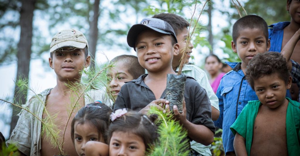 Sekelompok anak tersenyum di Guatemala menanam pohon bersama.