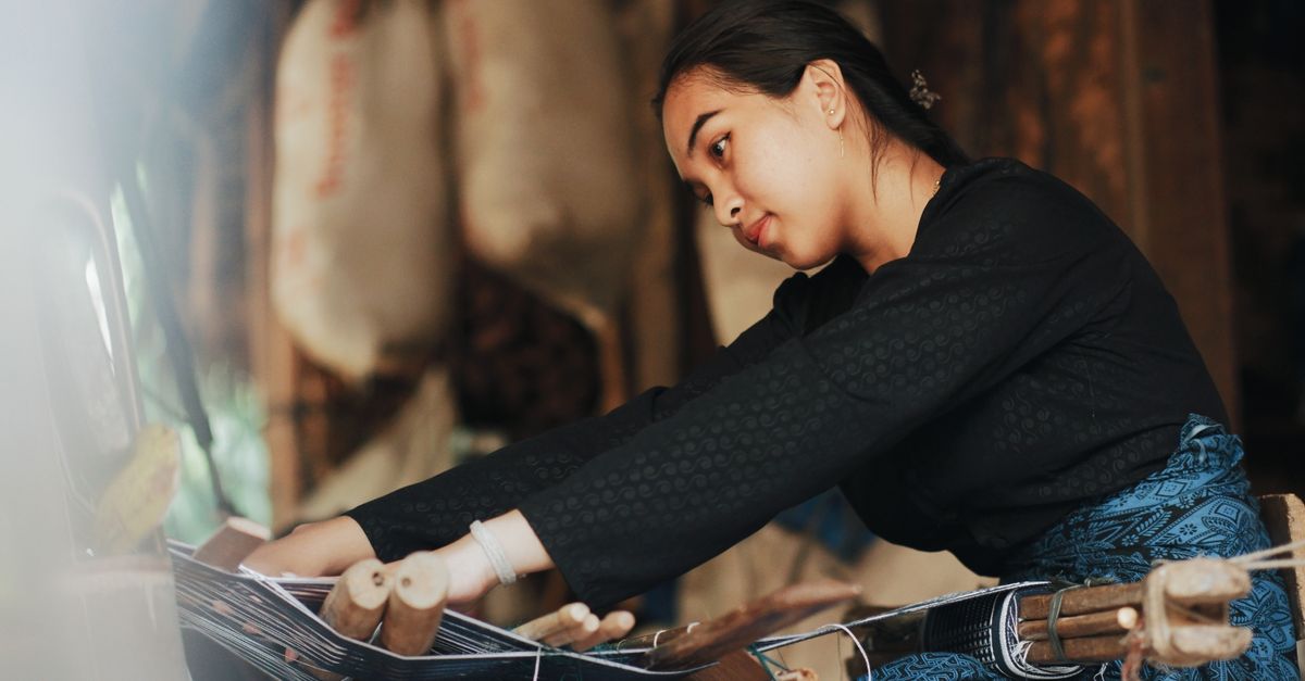 Seorang wanita dengan terampil menenun kain tradisional di atas alat tenun di Banten, Indonesia.