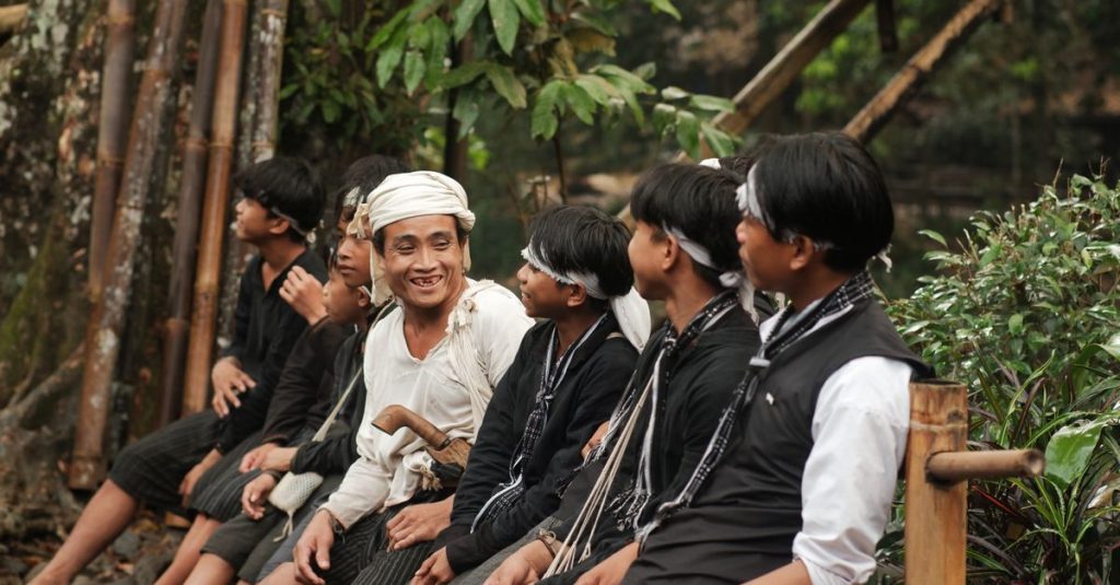 Sekelompok orang dewasa dalam pakaian tradisional berbagi momen gembira di alam yang rimbun di Banten, Indonesia.