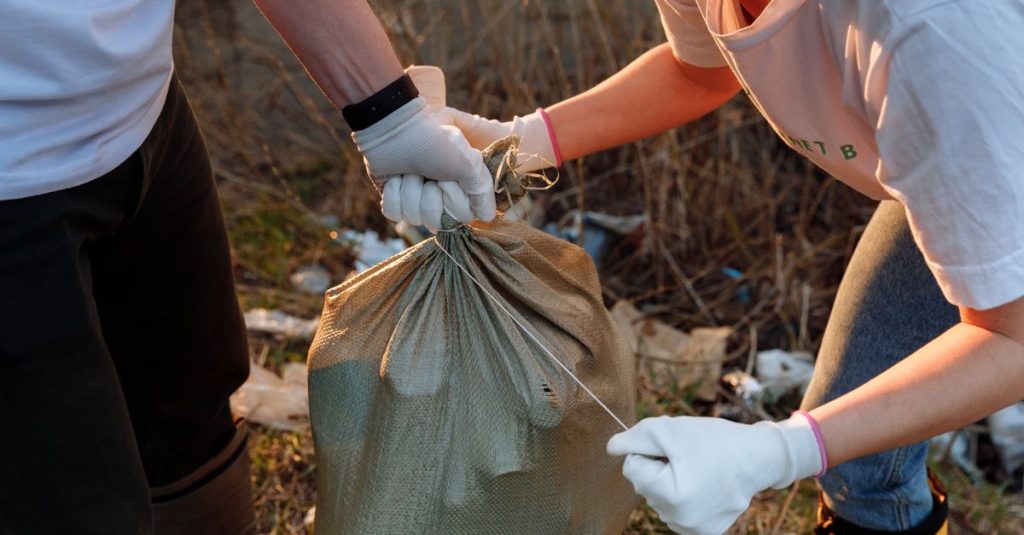 Dua orang mengikat karung sampah selama kegiatan pembersihan komunitas di luar ruangan.