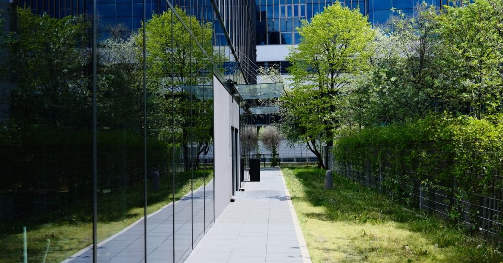 Gedung kaca modern dengan jalan setapak dan pepohonan, mencerminkan arsitektur perkotaan.