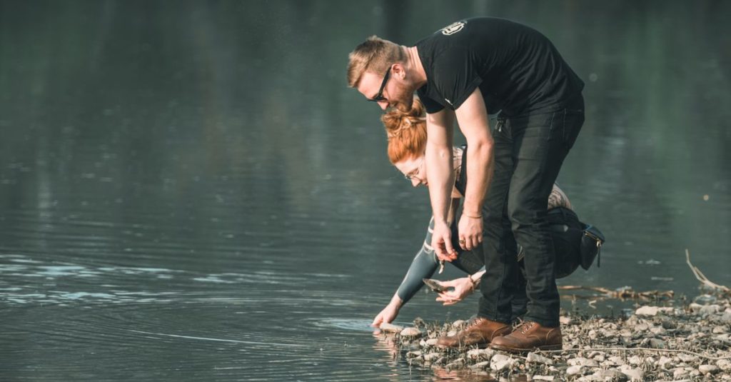 Sepasang kekasih berbagi momen damai di tepi danau, menjelajahi air di hari yang tenang.