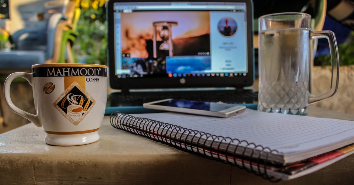 Pengaturan ruang kerja luar ruangan dengan kopi, laptop, dan buku catatan, ideal untuk pekerjaan jarak jauh.