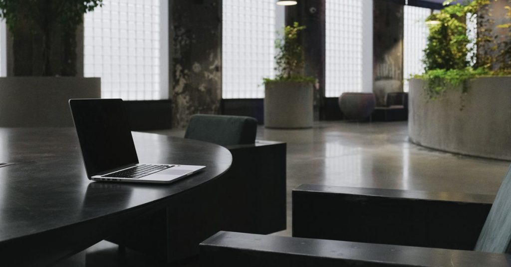 Interior kantor minimalis dengan laptop ramping di atas meja kayu dalam suasana yang stylish.