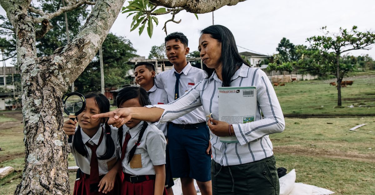 Siswa dengan seragam sekolah menjelajahi alam bersama guru mereka menggunakan kaca pembesar.