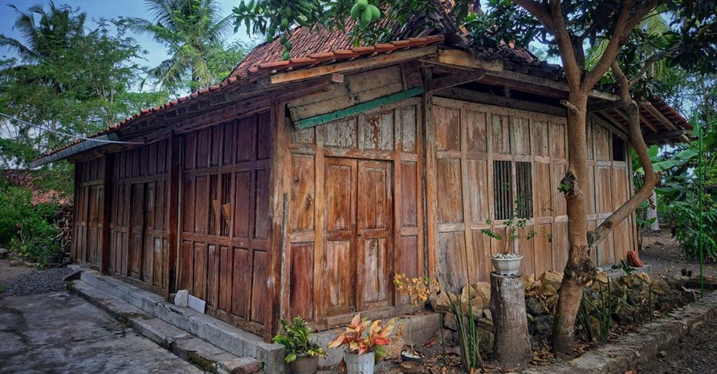 Bungalow kayu yang menawan dikelilingi oleh pepohonan dan kehijauan dalam suasana pedesaan yang tenang.