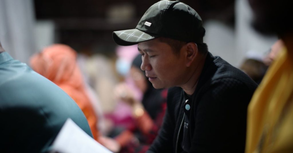 Pria Asia dengan topi hitam membaca dengan seksama di dalam ruangan di Jakarta Barat.
