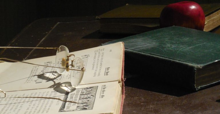 Koleksi buku vintage dan kacamata di atas meja kayu, menciptakan suasana nostalgic.