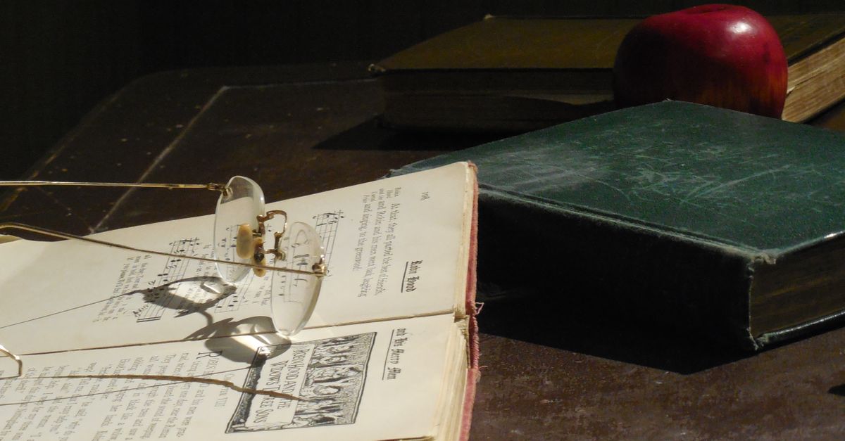 Koleksi buku vintage dan kacamata di atas meja kayu, menciptakan suasana nostalgic.