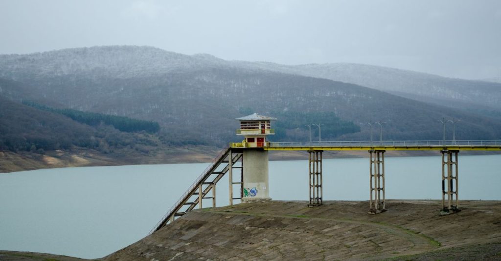 Pemandangan tenang Waduk Sioni dengan menara air arsitektur dan perbukitan sekitarnya.