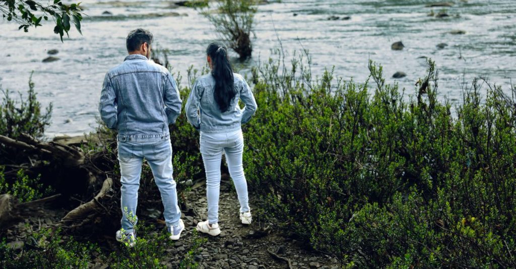 Sekelompok pasangan mengenakan jaket denim berdiri di tepi sungai yang subur, menikmati alam.