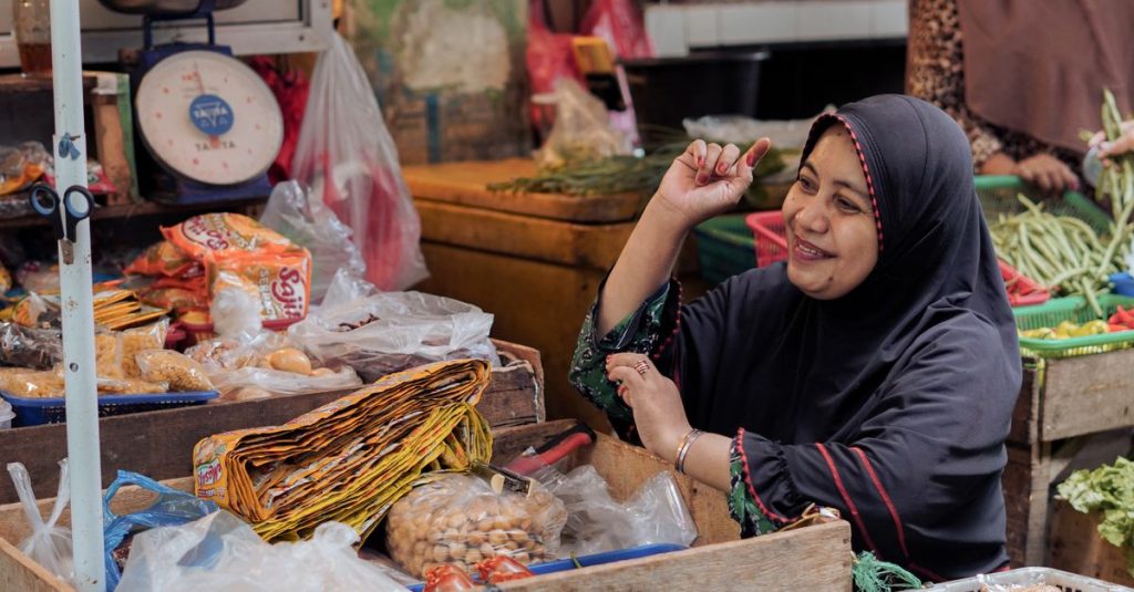 Seorang penjual yang tersenyum dengan hijab di pasar yang ramai di Pontianak, Indonesia.