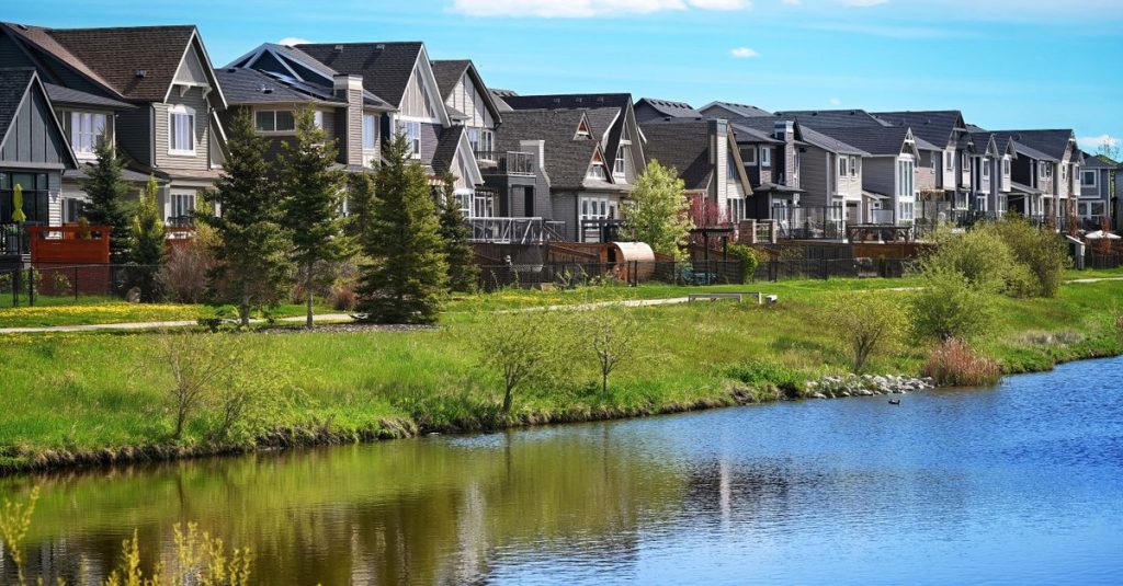 Rumah-rumah modern di pinggiran kota yang berjejer di tepi kolam yang tenang di Airdrie, Alberta, Kanada.