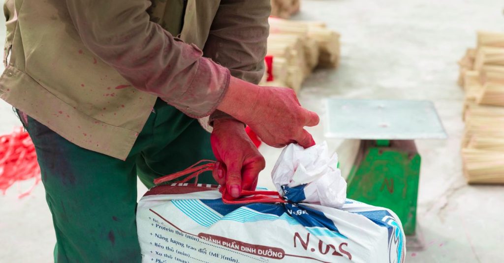 Close-up seorang pria mengikat paket di lingkungan industri, menampilkan kerja manual dan logistik.