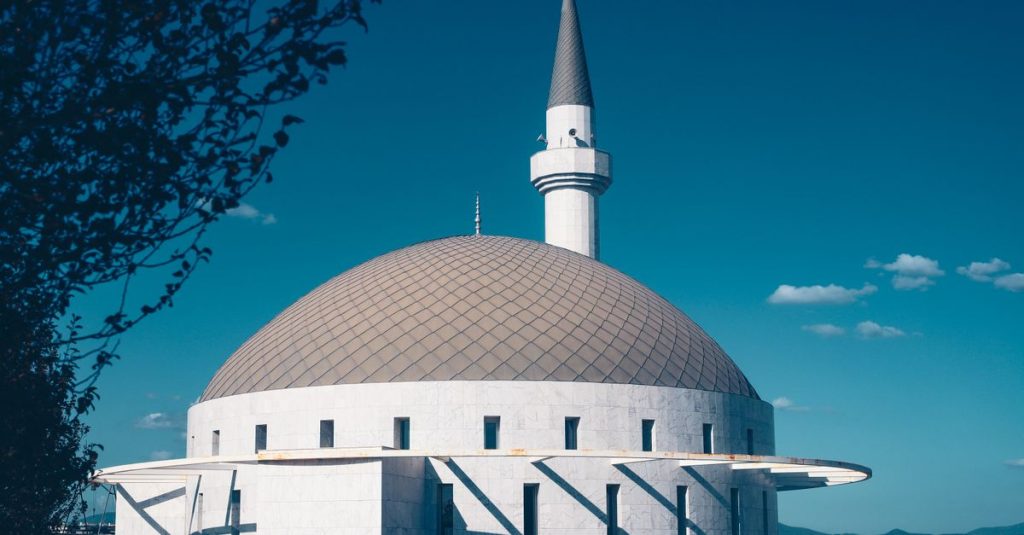 Sebuah masjid modern yang menampilkan kubah dan menara yang khas di latar belakang langit biru cerah.