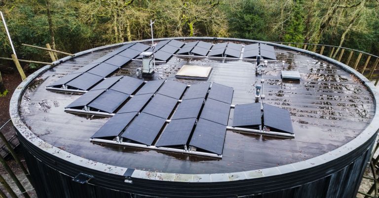 Pemandangan udara dari atap bulat dengan panel surya dikelilingi pepohonan, mempromosikan energi terbarukan.
