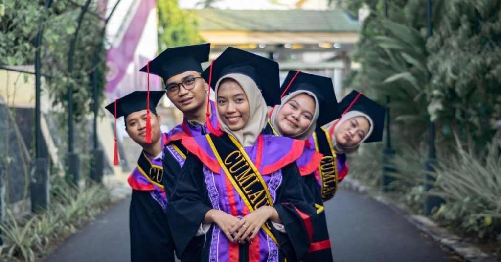 Lulusan yang ceria mengenakan topi dan toga merayakan kesuksesan mereka di luar ruangan.
