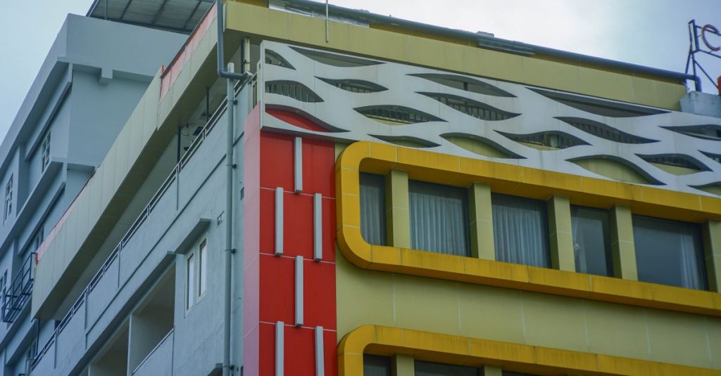 Tampilan dekat fasad bangunan modern yang menampilkan elemen merah, kuning, dan putih di lingkungan perkotaan.