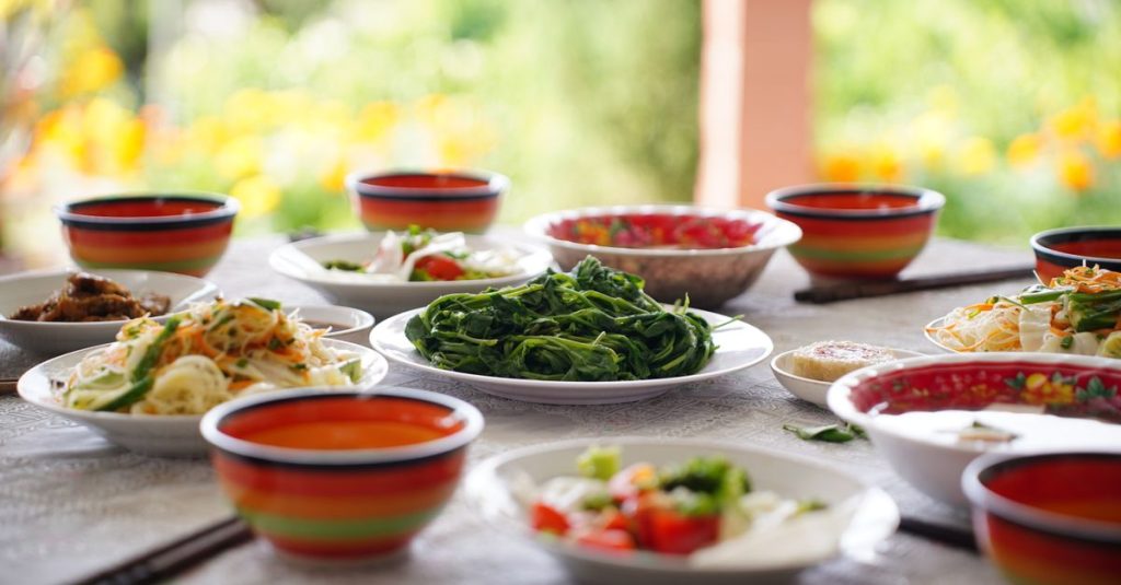 Meja berisi salad dan sayuran segar khas Asia di luar ruangan, mangkuk warna-warni memperindah suasana.