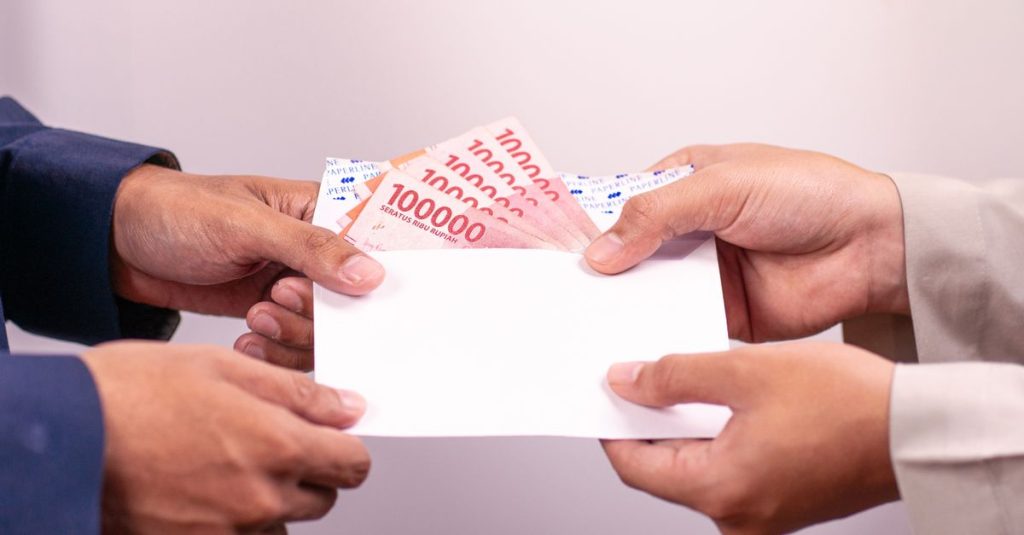 Tangan menukar amplop dengan Rupiah Indonesia, menyoroti transaksi keuangan.