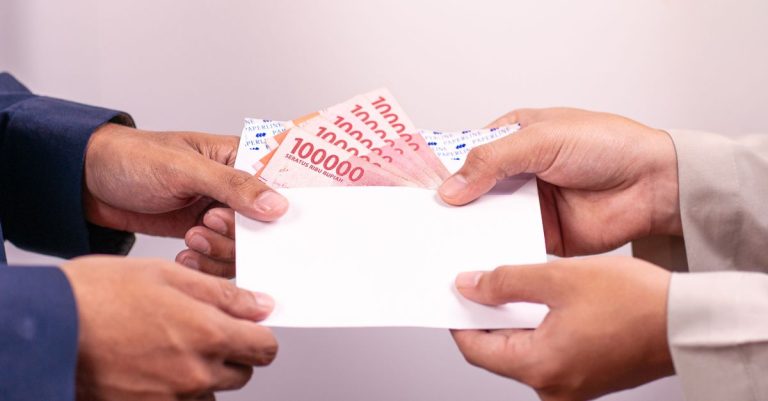 Tangan menukar amplop dengan Rupiah Indonesia, menyoroti transaksi keuangan.