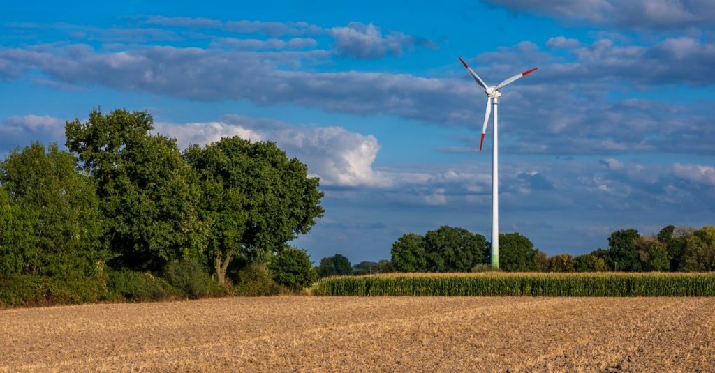 Turbin angin di ladang pedesaan yang cerah dengan langit biru, melambangkan energi terbarukan.