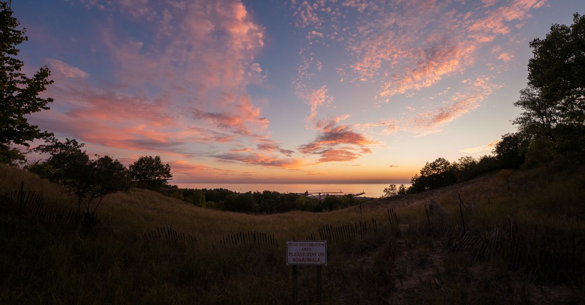 Matahari terbenam yang dramatis di atas bukit pasir Gunung Pisgah di Holland, Michigan dengan awan berwarna-warni dan pemandangan yang tenang.