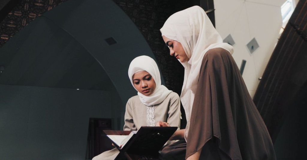 Dua wanita Muslim membaca Al-Qur'an di lingkungan masjid yang tenang di Bandung, Indonesia.