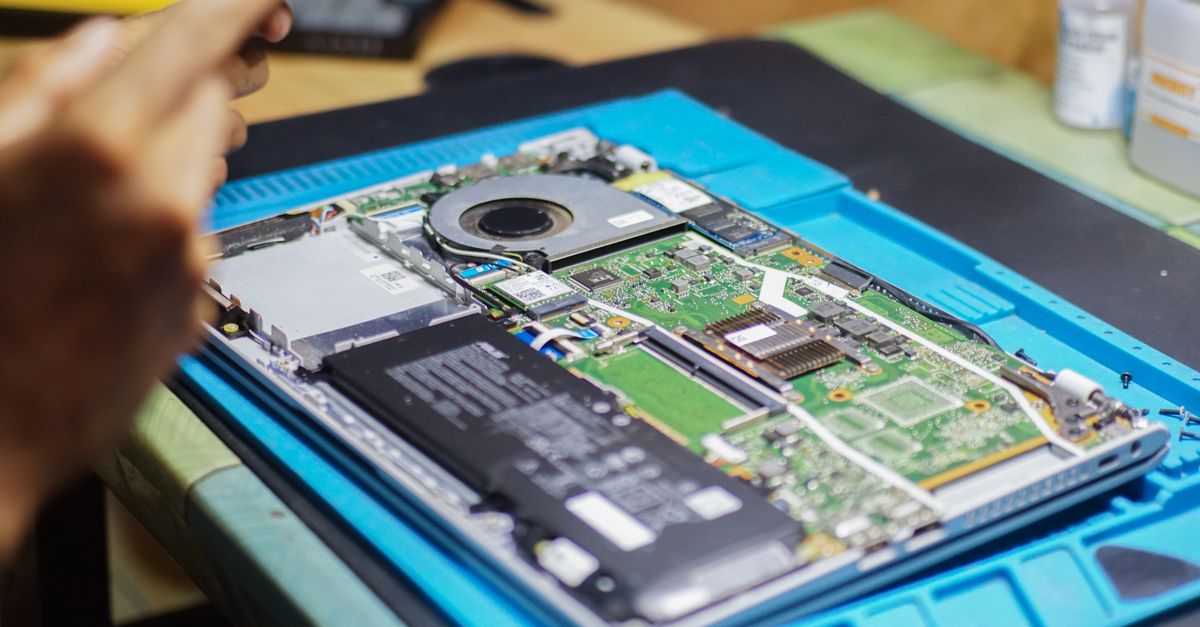 Tampilan dekat laptop yang sedang diperbaiki dengan komponen dan peralatan yang terlihat.