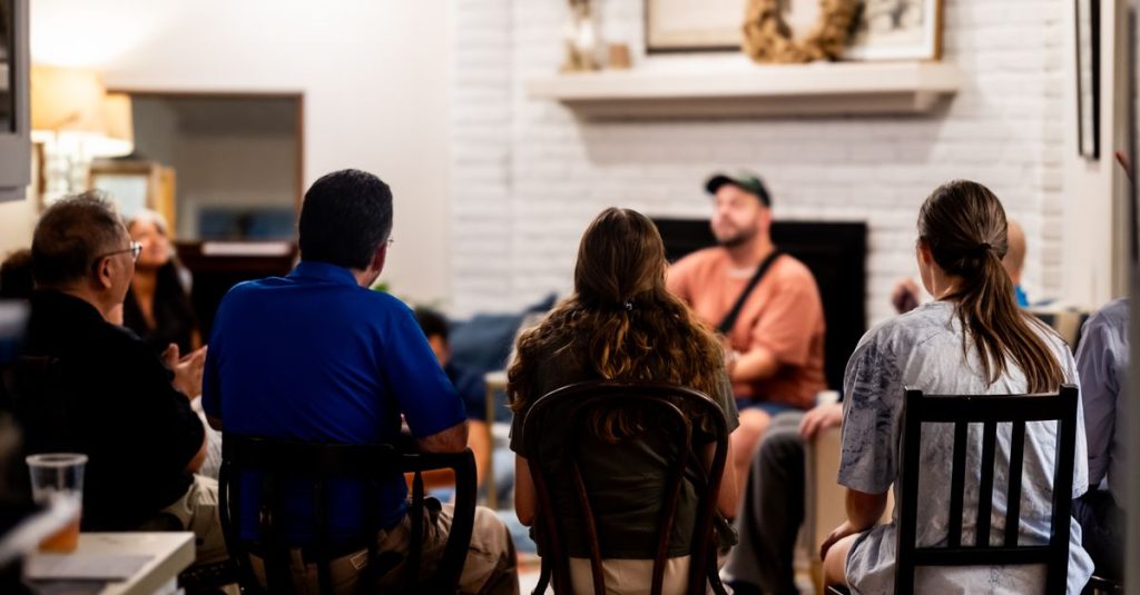 Sekelompok orang yang beragam terlibat dalam percakapan santai di ruang tamu yang nyaman.