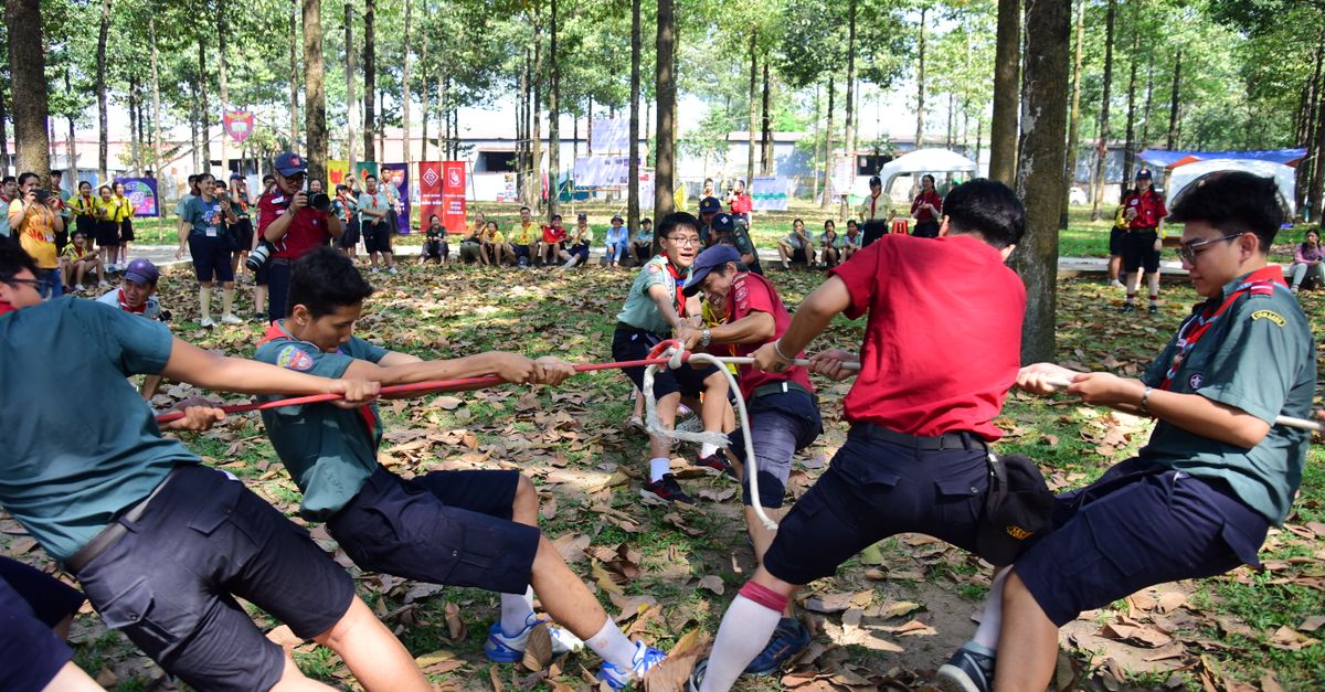 Sekelompok remaja bermain tarik tambang di area berhutan selama perkemahan pramuka.