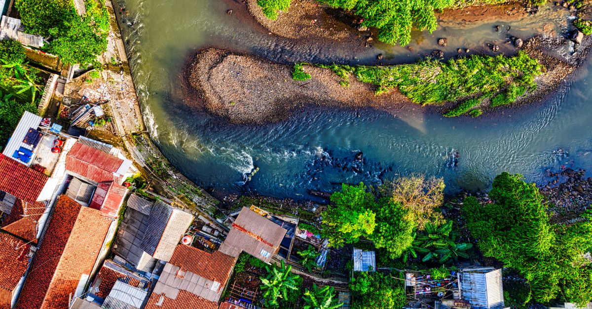 Pandangan udara yang cerah dari sungai yang berkelok-kelok melalui desa hijau yang subur di Jawa Barat, Indonesia.