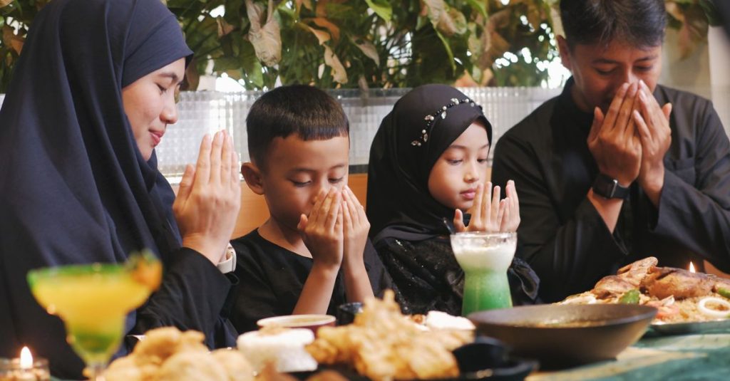Sebuah keluarga berkumpul di dalam ruangan untuk makan malam tradisional Ramadan, berdoa bersama.