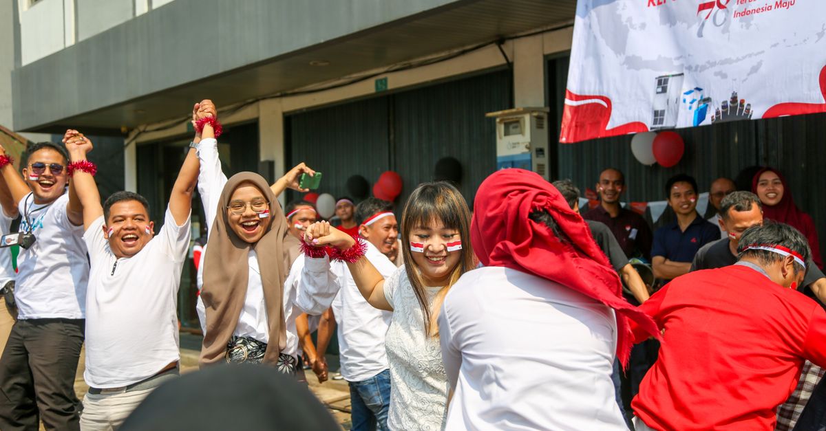 Perayaan luar ruangan yang penuh kegembiraan untuk Hari Kemerdekaan Indonesia dengan orang-orang yang bermain permainan tradisional.