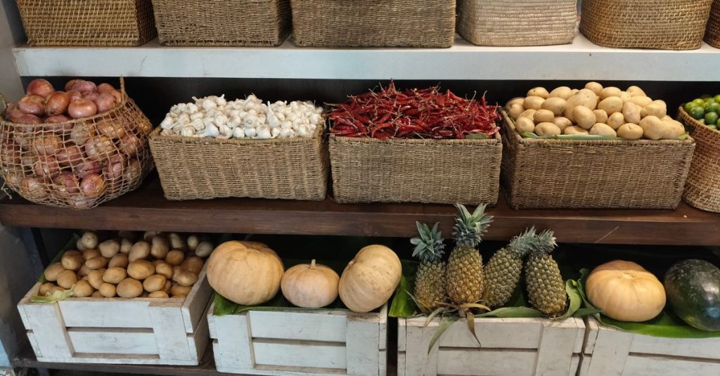 Tampilan pasar yang semarak menampilkan beragam sayuran dan buah-buahan segar dalam keranjang anyaman dan peti kayu.