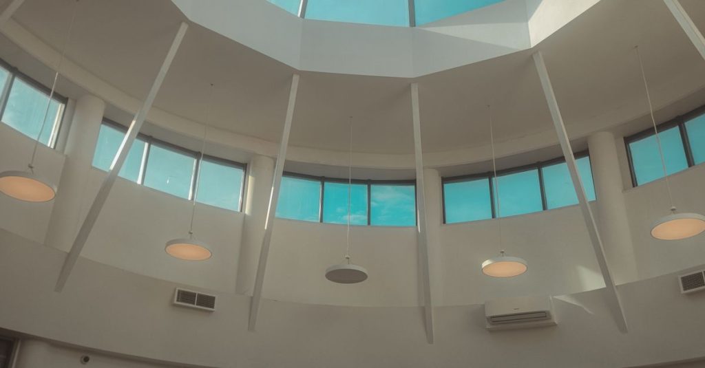Pemandangan interior langit-langit kubah modern dengan jendela atap melingkar dan lampu gantung.