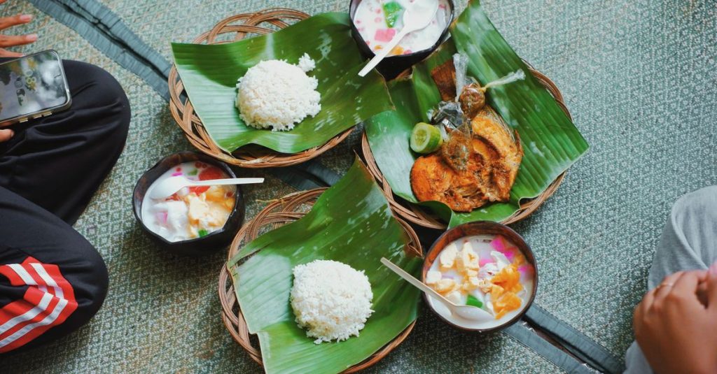 Nikmati hidangan tradisional Indonesia yang terdiri dari nasi, ikan, dan makanan penutup yang disajikan di atas daun pisang.