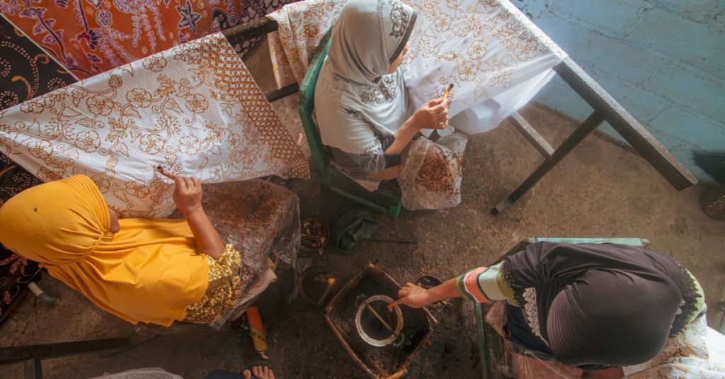 Para wanita membuat batik tradisional menggunakan metode lilin di Indonesia, menampilkan warisan budaya.
