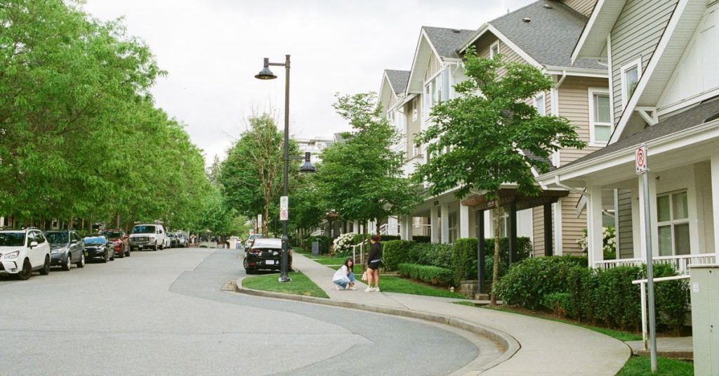 Jalan Vancouver yang menawan dengan keluarga menikmati hari di luar ruangan di antara pohon-pohon dan rumah-rumah. Adegan komunitas perkotaan.