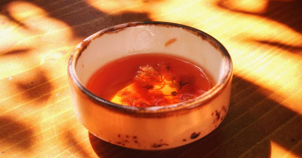 Cangkir keramik dengan teh herbal yang menangkap sinar matahari, menciptakan suasana hangat dan tenang.