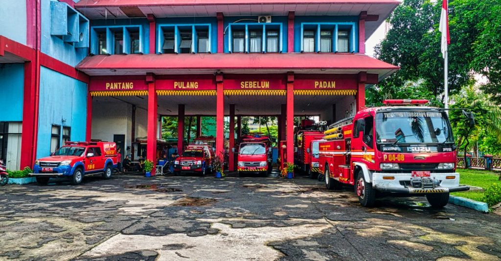 Mobil pemadam kebakaran diparkir di depan sebuah stasiun pemadam kebakaran yang cerah di Jakarta, Indonesia.