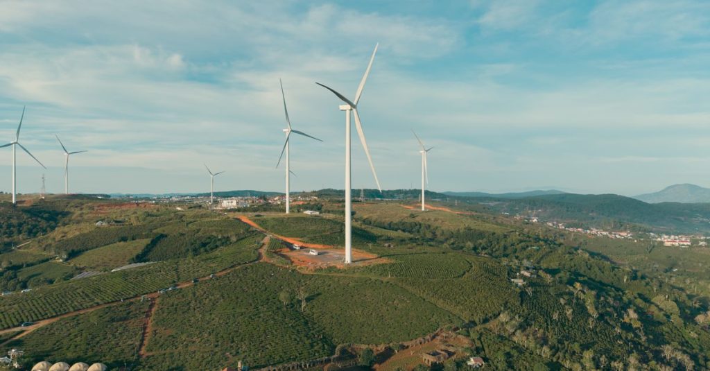Pemandangan udara ladang angin di perbukitan hijau yang bergelombang, menampilkan energi terbarukan yang selaras dengan alam.