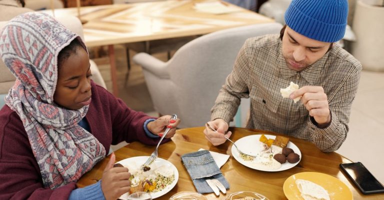 Pasangan multietnis yang makan di dalam ruangan, menikmati hidangan Timur Tengah.