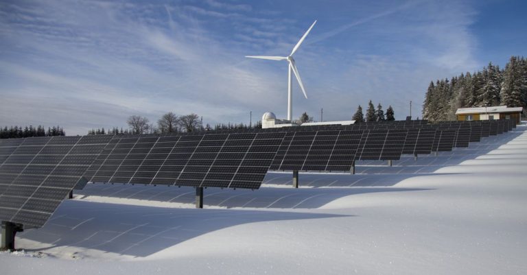 Panel surya dan turbin angin di lanskap bersalju yang menampilkan sumber energi terbarukan.