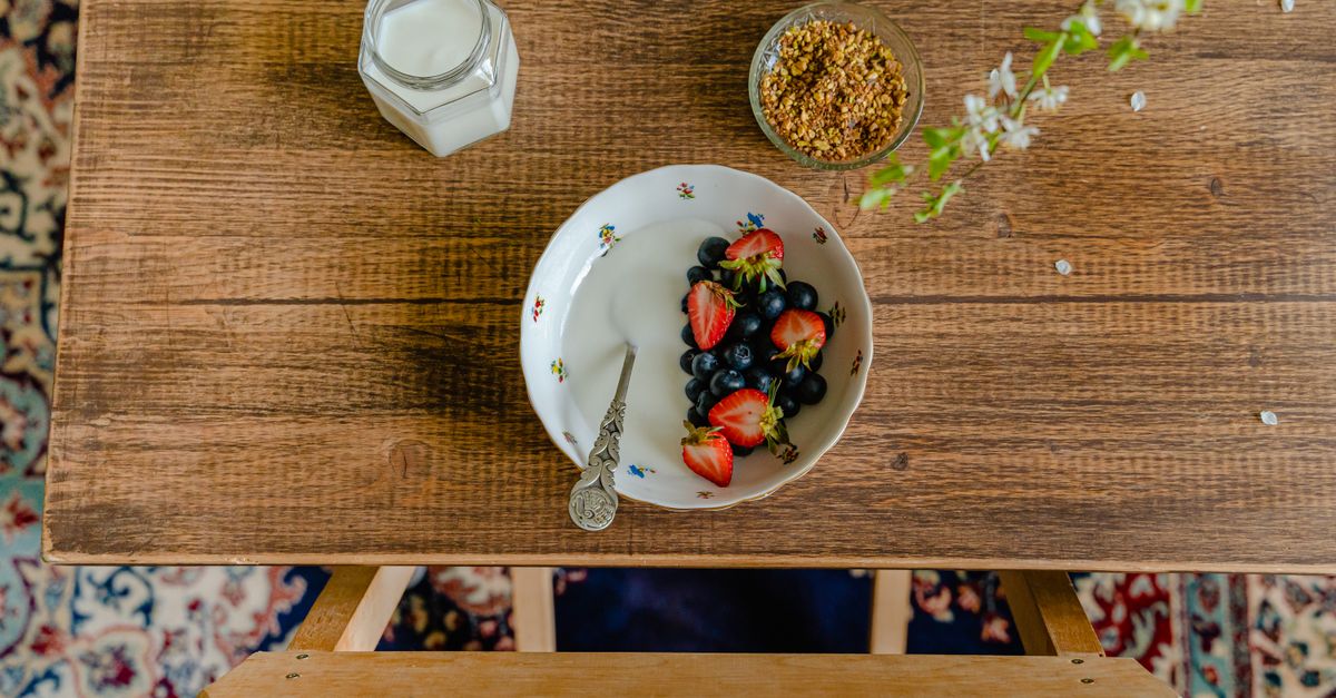 Pandangan udara dari pengaturan sarapan dengan mangkuk buah segar, susu, dan granola di atas meja kayu.