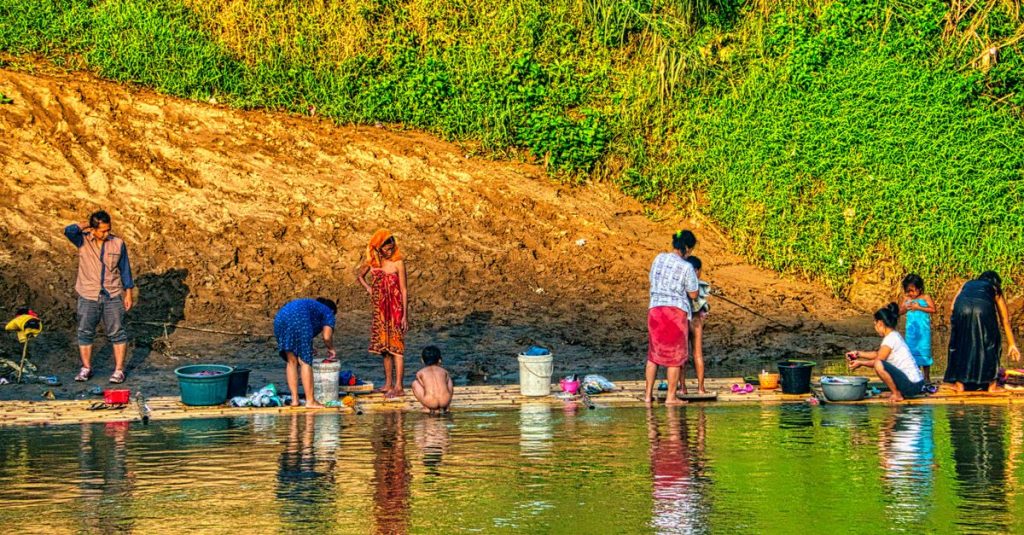 Sekelompok orang yang mencuci pakaian dan mandi di tepi sungai di pedesaan Indonesia.
