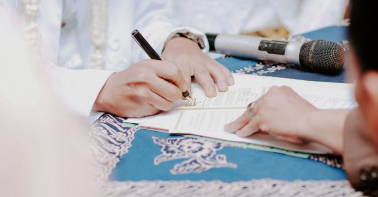 Close-up tangan menandatangani dokumen pernikahan dengan mikrofon di atas meja.
