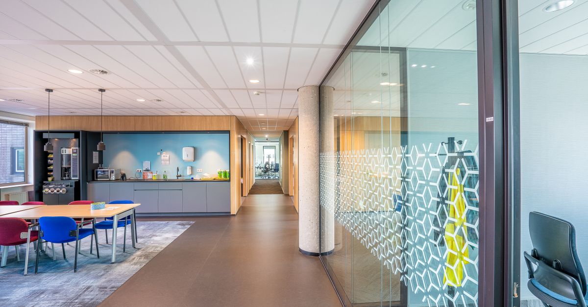 Ruang kantor modern yang ramping dengan tempat duduk berwarna-warni dan dapur kecil dalam lingkungan yang cerah dan terang.