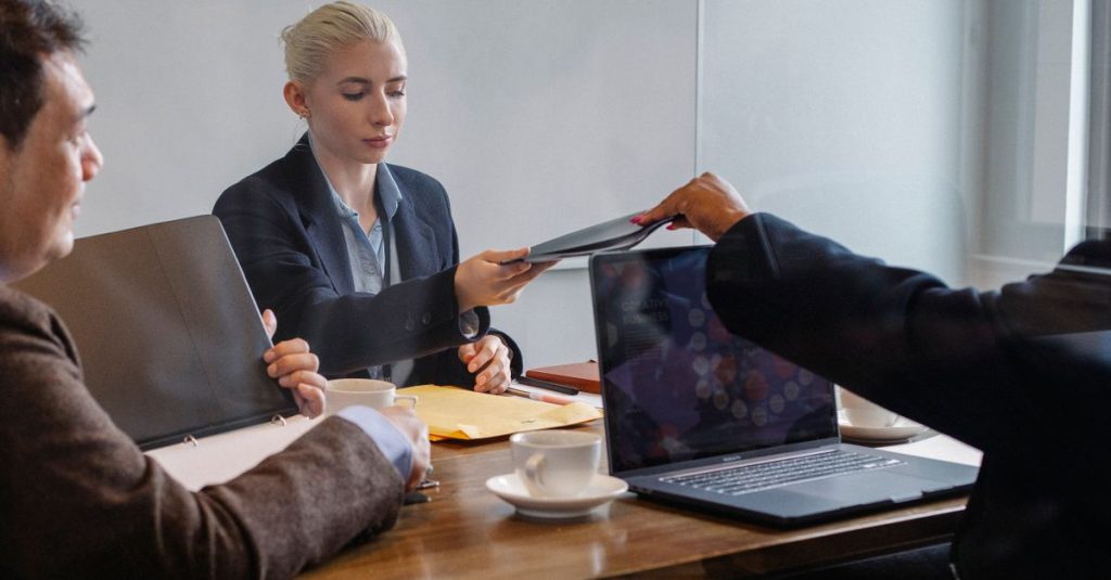 Sekelompok profesional yang beragam di lingkungan kantor modern, berbagi dokumen dan menggunakan laptop.